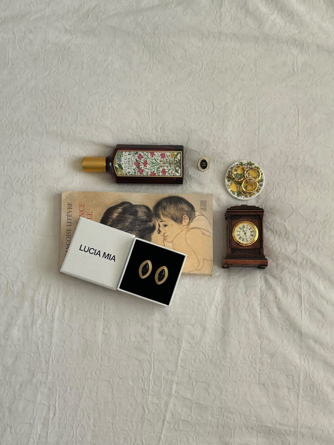 Collection of items including a bottle, book, clock, and jewelry on a textured surface